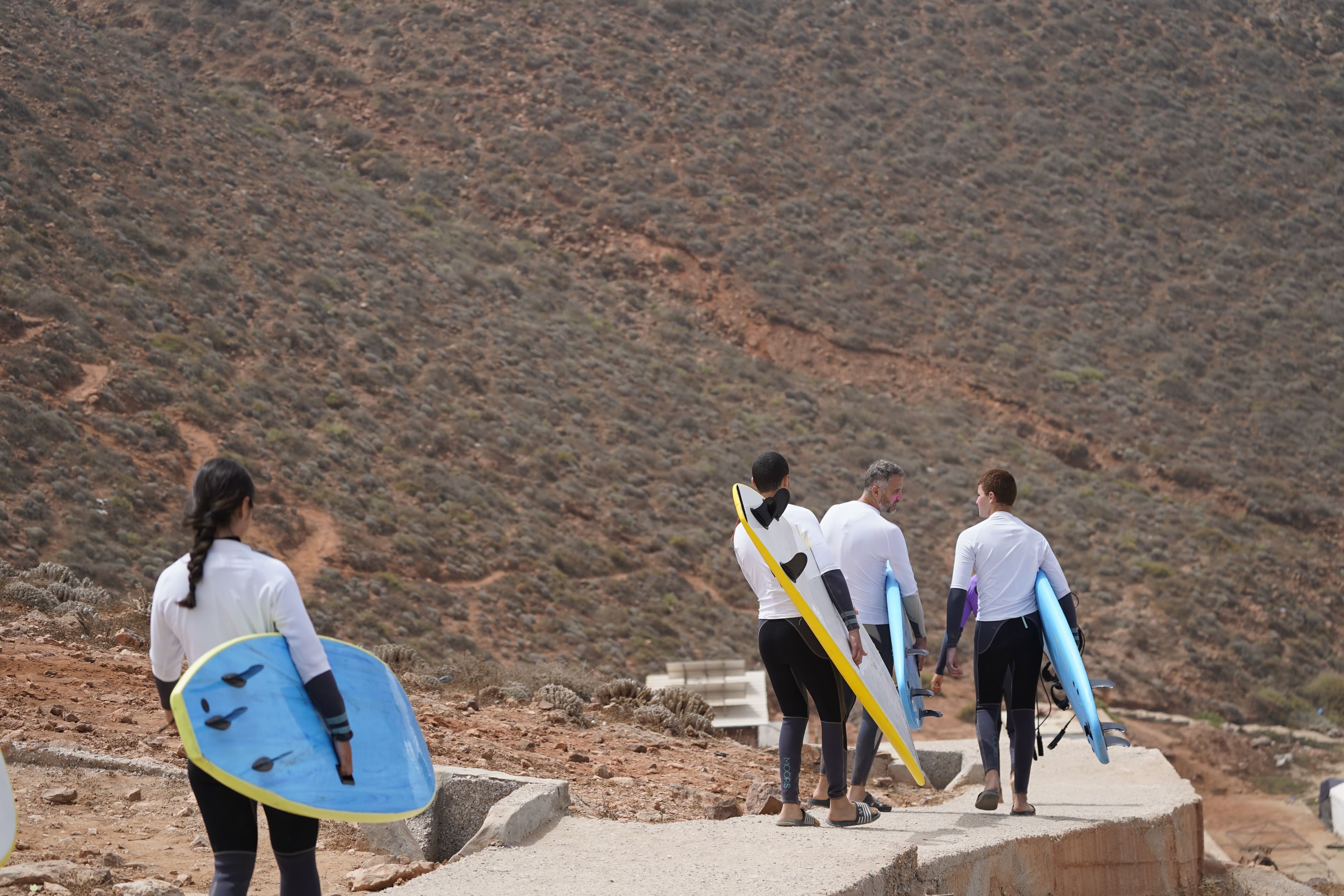 Surf group carrying boards toward a Mirleft surf spot